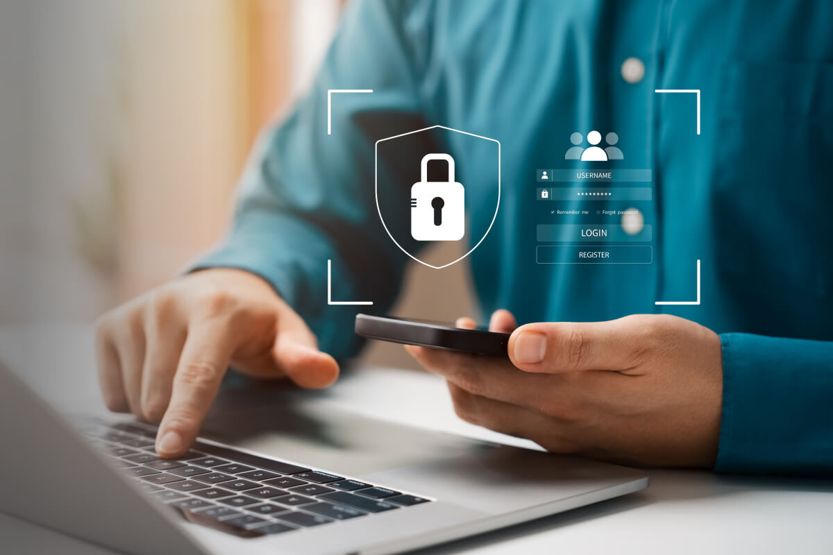 A person's hands configuring security settings using a smartphone and a laptop.